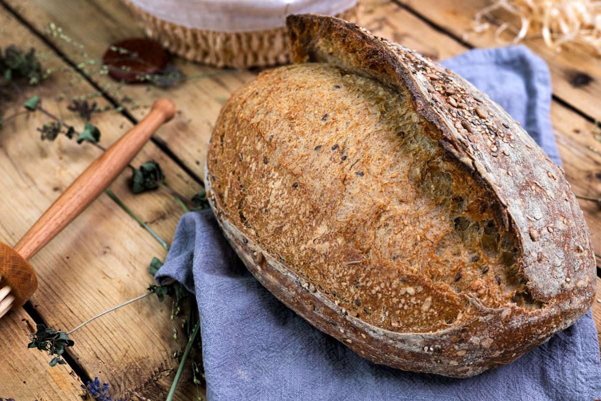 Pagnotta a lievitazione naturale con crosta dorata e semi su tavolo di legno