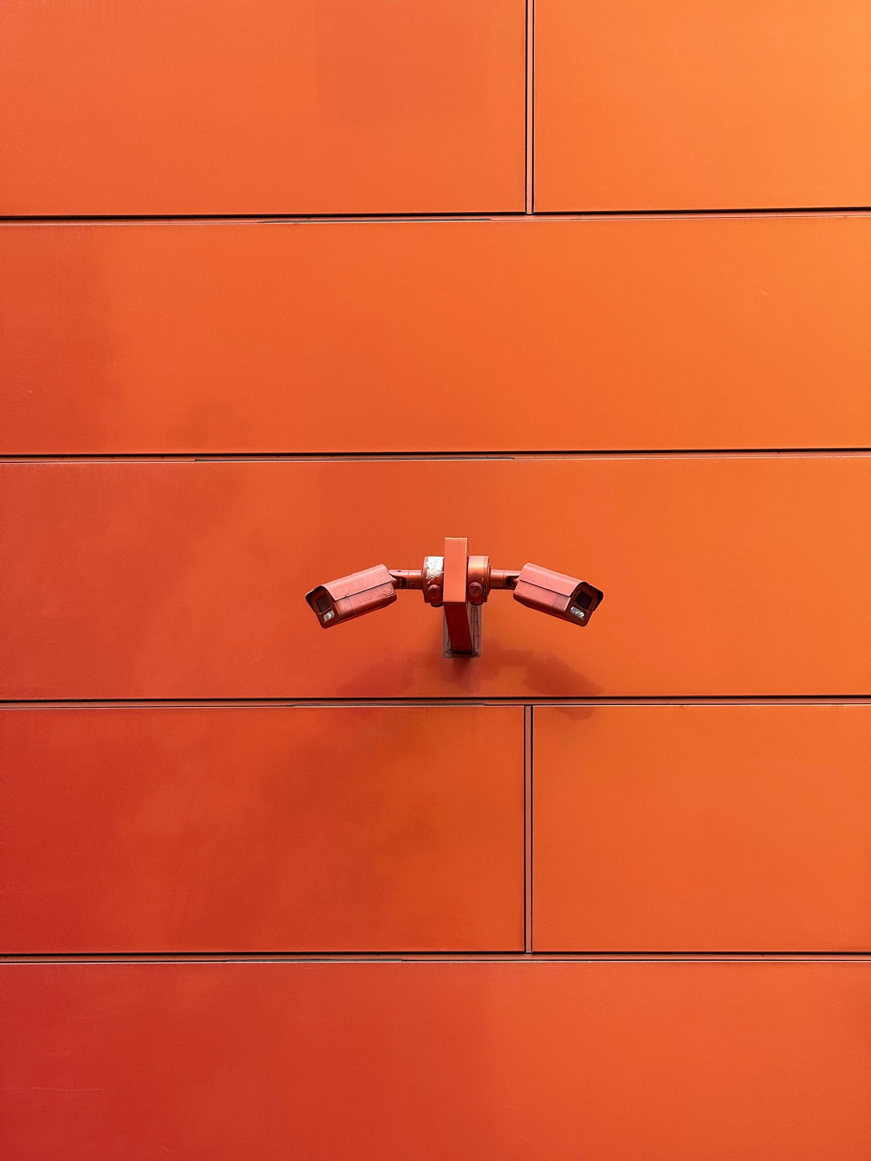 Zadarmo Dve CCTV kamery namontované na žiarivo oranžovej stene, ktoré predstavujú moderný dohľad. Fotka z fotobanky