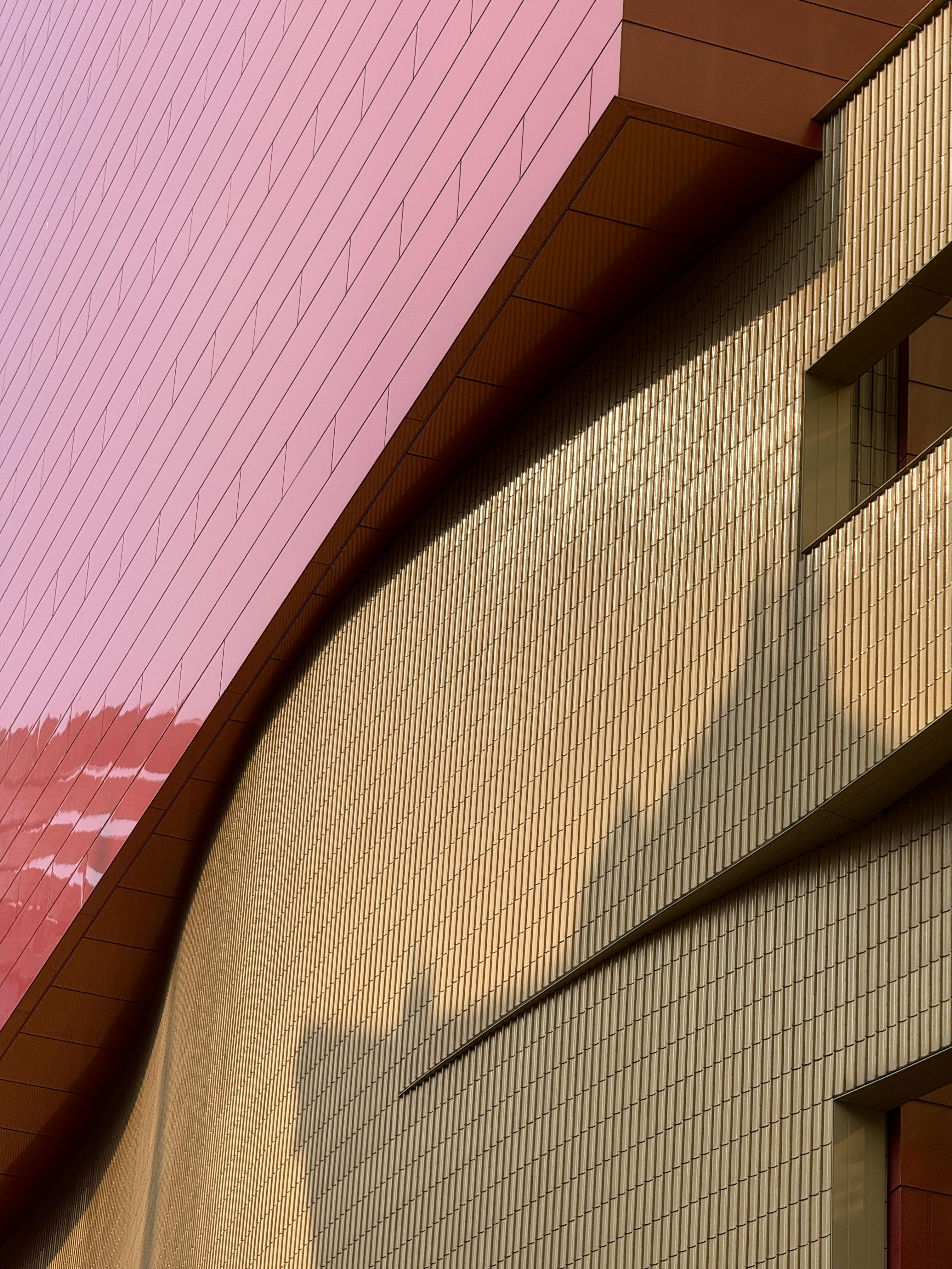 Abstract view of a modern building with pink and gold exterior featuring geometric patterns.