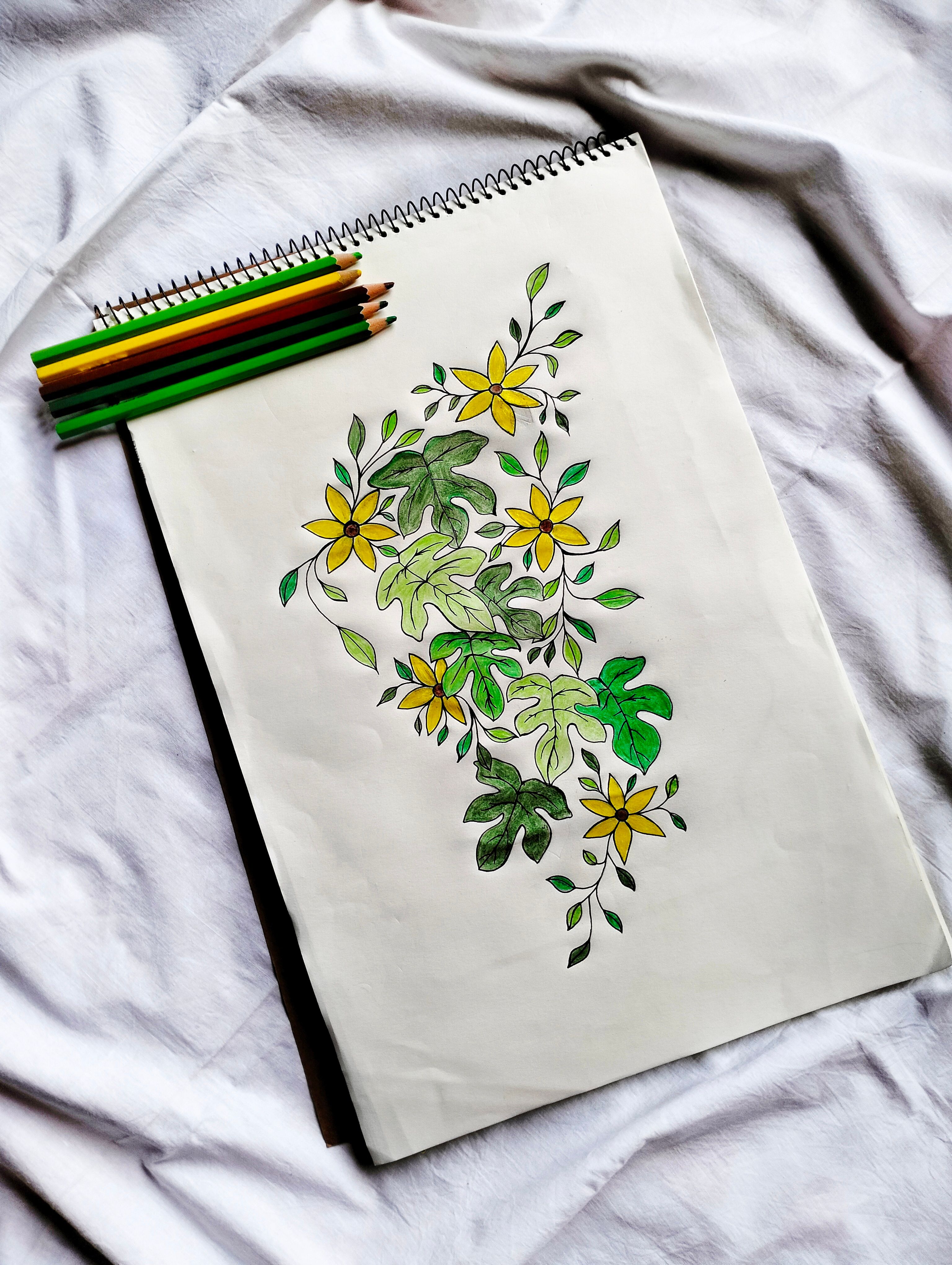 Artistic sketch of yellow flowers and green leaves on a notepad with colored pencils.