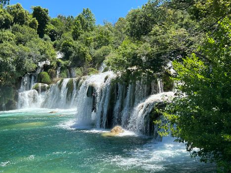 Beautiful cascading waterfall surrounded by lush greenery under clear blue skies.