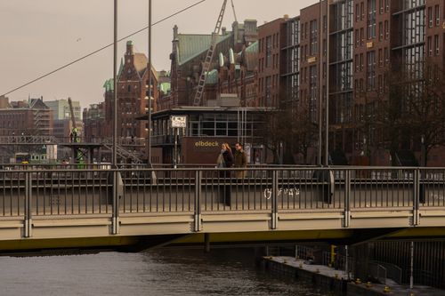 Free A couple walks on a bridge in Hamburg's historic Speicherstadt district, with iconic warehouses in the background. Stock Photo