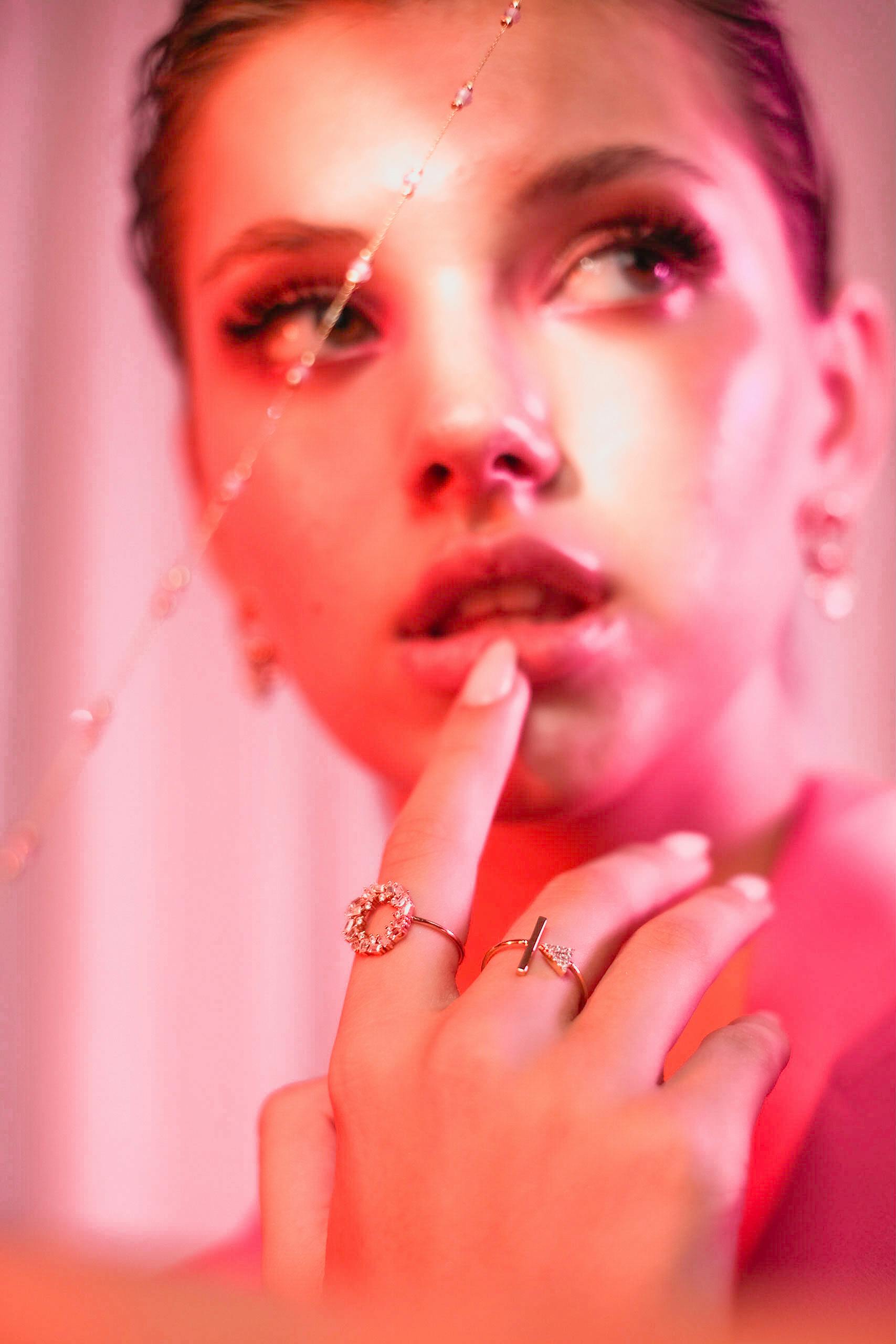 bezplatná Detailní portrét ženy ozdobené elegantními šperky pod dramatickým růžovým osvětlením. Základová fotografie