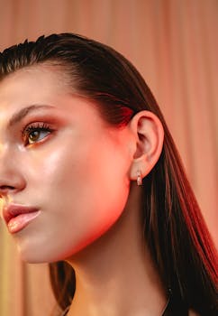 Stylish close-up portrait of a woman with sleek hair and a sparkling earring under soft red lighting.