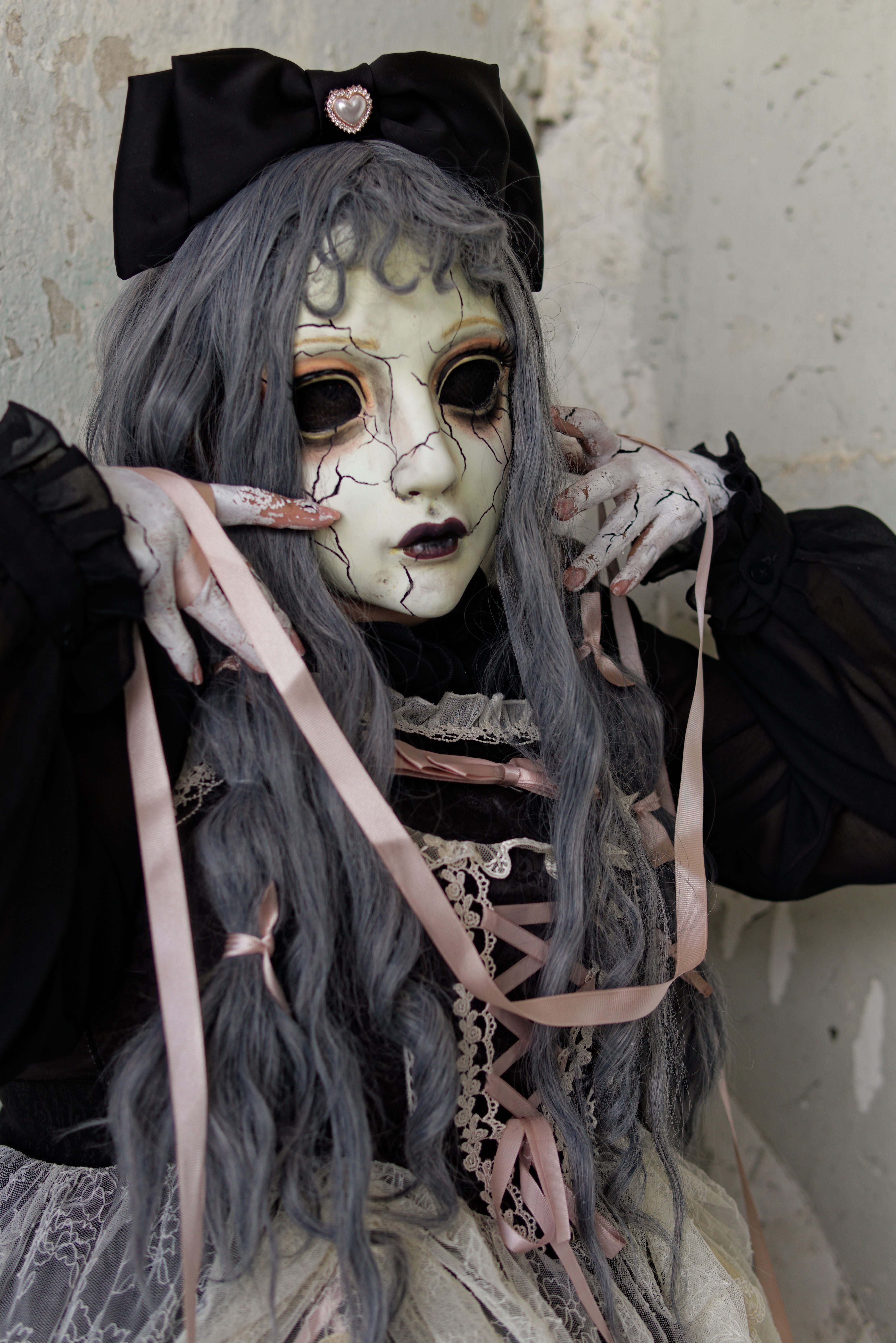 Spooky doll-like figure with crackled makeup, eerie look, and pastel ribbons in a black Gothic dress.