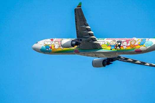 Airplane with vibrant cartoon characters flying against a clear blue sky.