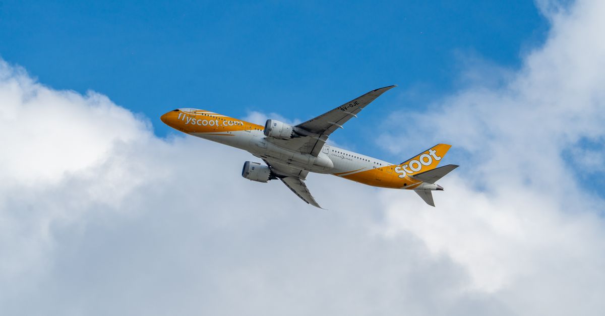 Photo by Wei86 Travel A flyscoot airplane soaring through a clear blue sky with fluffy clouds.