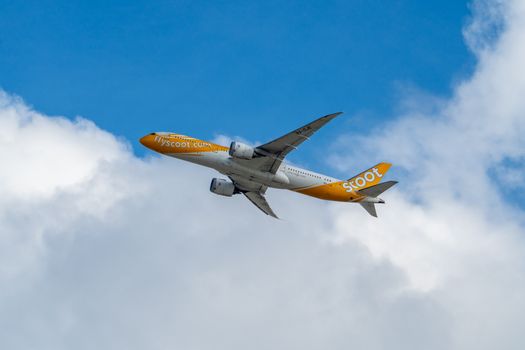 Photo by Wei86 Travel A flyscoot airplane soaring through a clear blue sky with fluffy clouds.