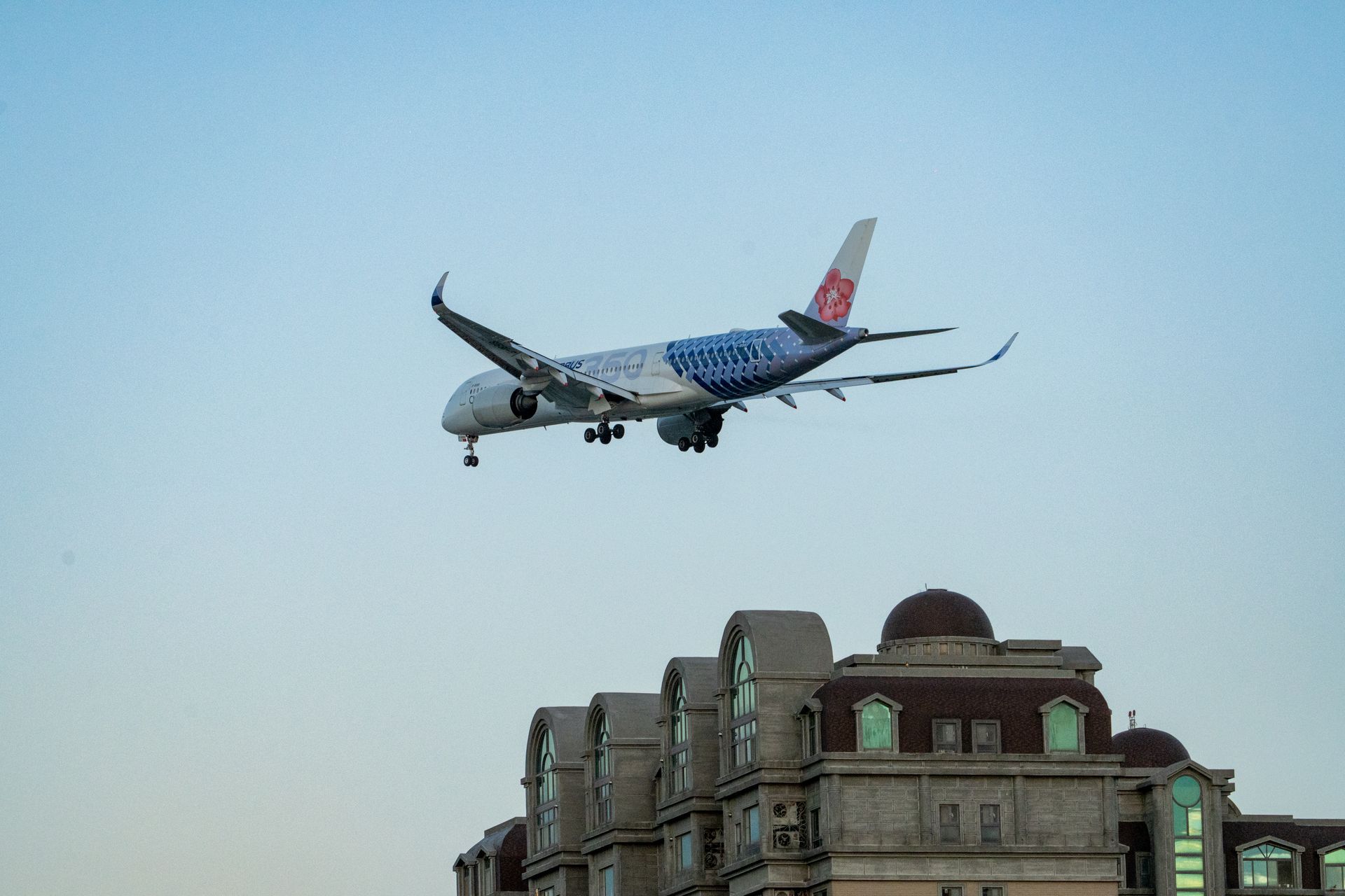 A commercial aircraft approaches for landing over urban buildings with a clear sky.
