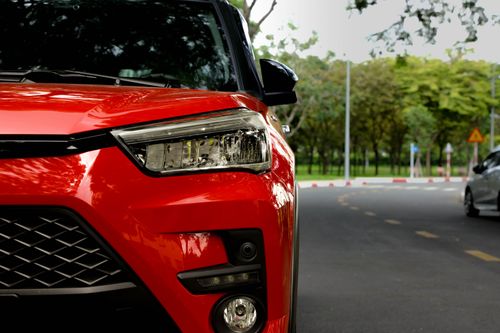 Free Close-up of a red car on a city street with lush green trees in the background. Stock Photo