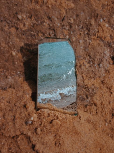 A unique reflection of waves on a beach captured in a broken mirror on the sand.