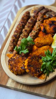A delicious assortment of grilled meats and vegetables on a wooden platter with fresh herbs.