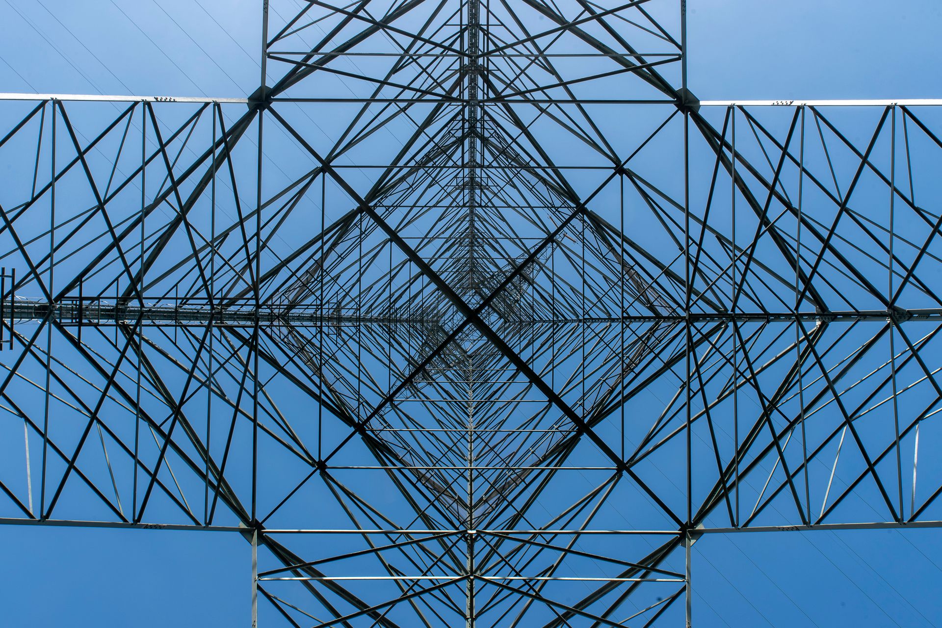 Artistic perspective of a power line tower showing geometric symmetry against a clear blue sky.