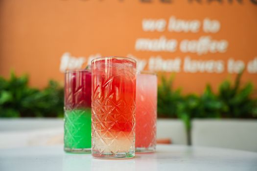 Colorful cocktails in crystal glasses on an outdoor table with decorative background.