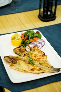 Delicious grilled fish served with fresh salad and lemon on a white plate.