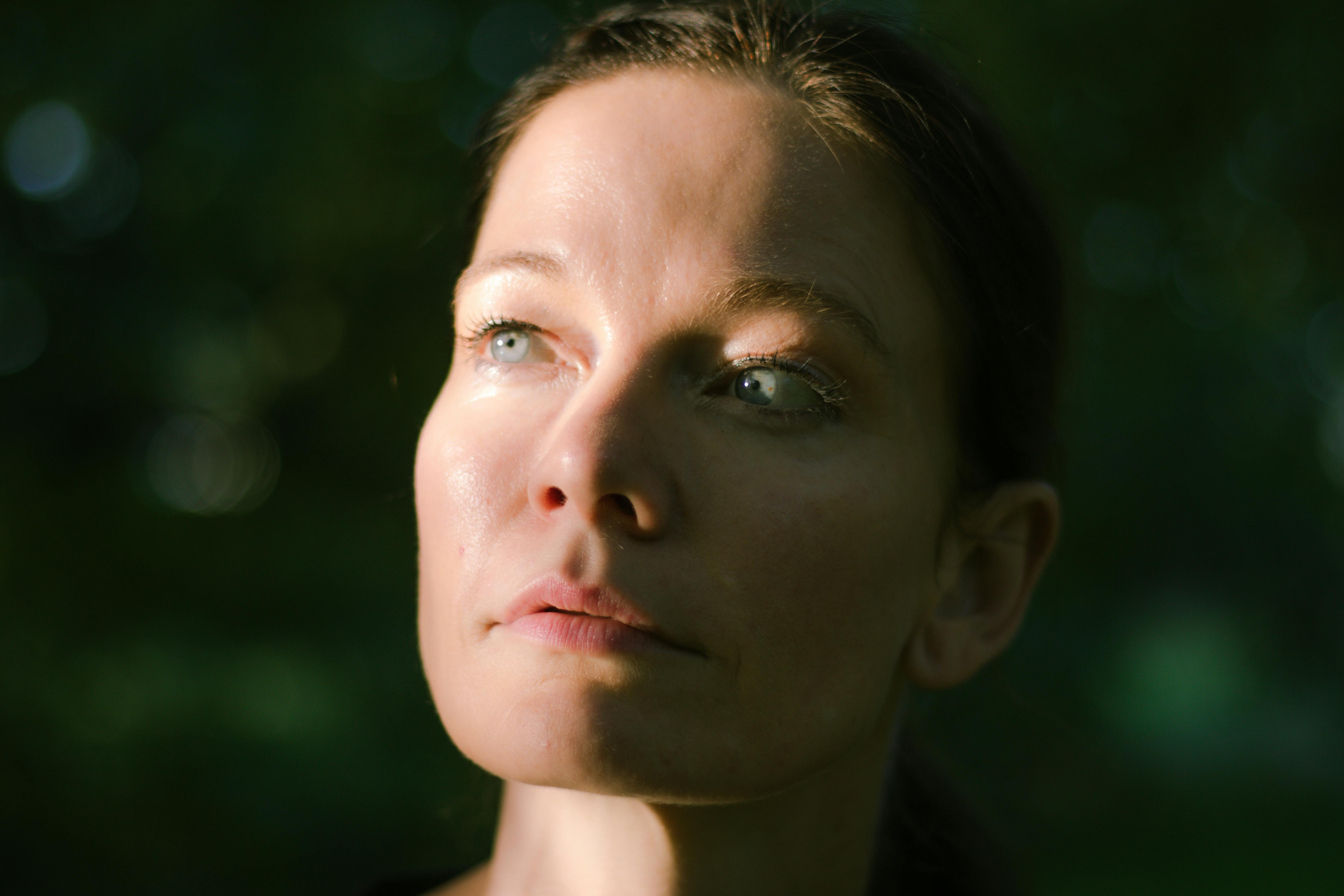 A contemplative woman looks upward in a serene outdoor setting with soft natural lighting.