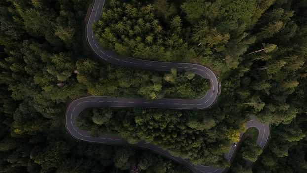 Luchtfoto van een kronkelende weg door een dicht, groen bos.