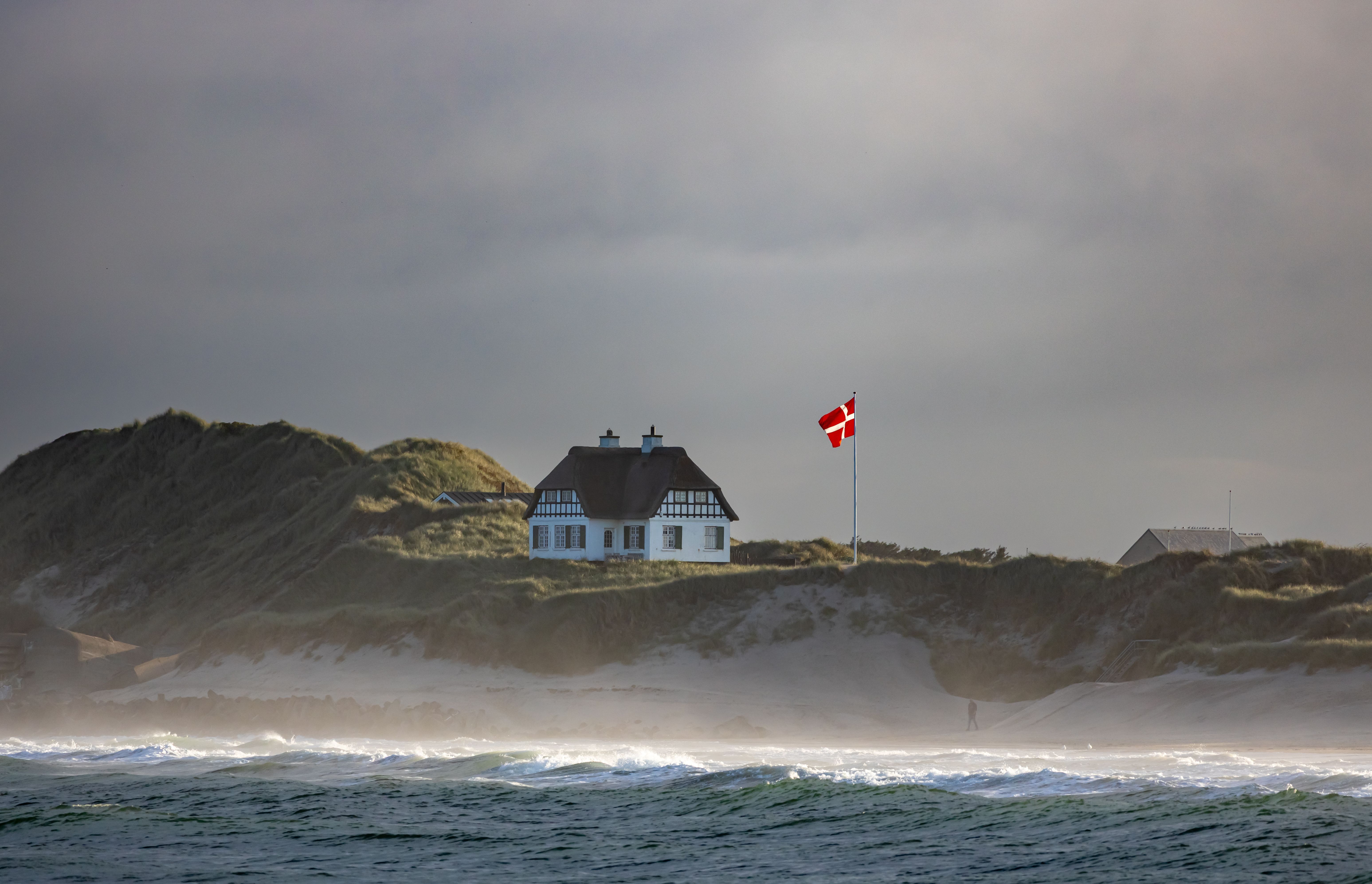 Charmant cottage sur la côte danoise avec drapeau flottant et vagues déferlantes.