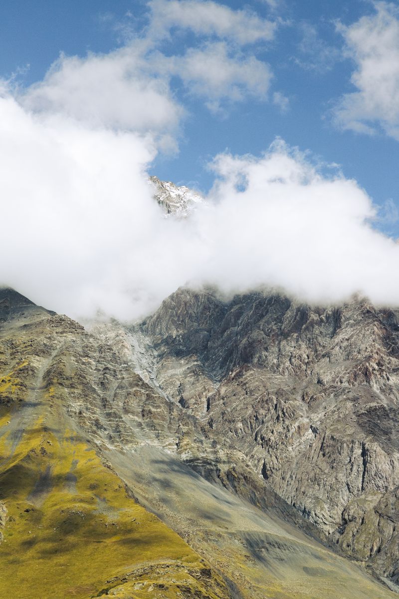 Breathtaking view of Kazbegi Mountains in Georgia with clouds partially covering the peaks, captured during summer.