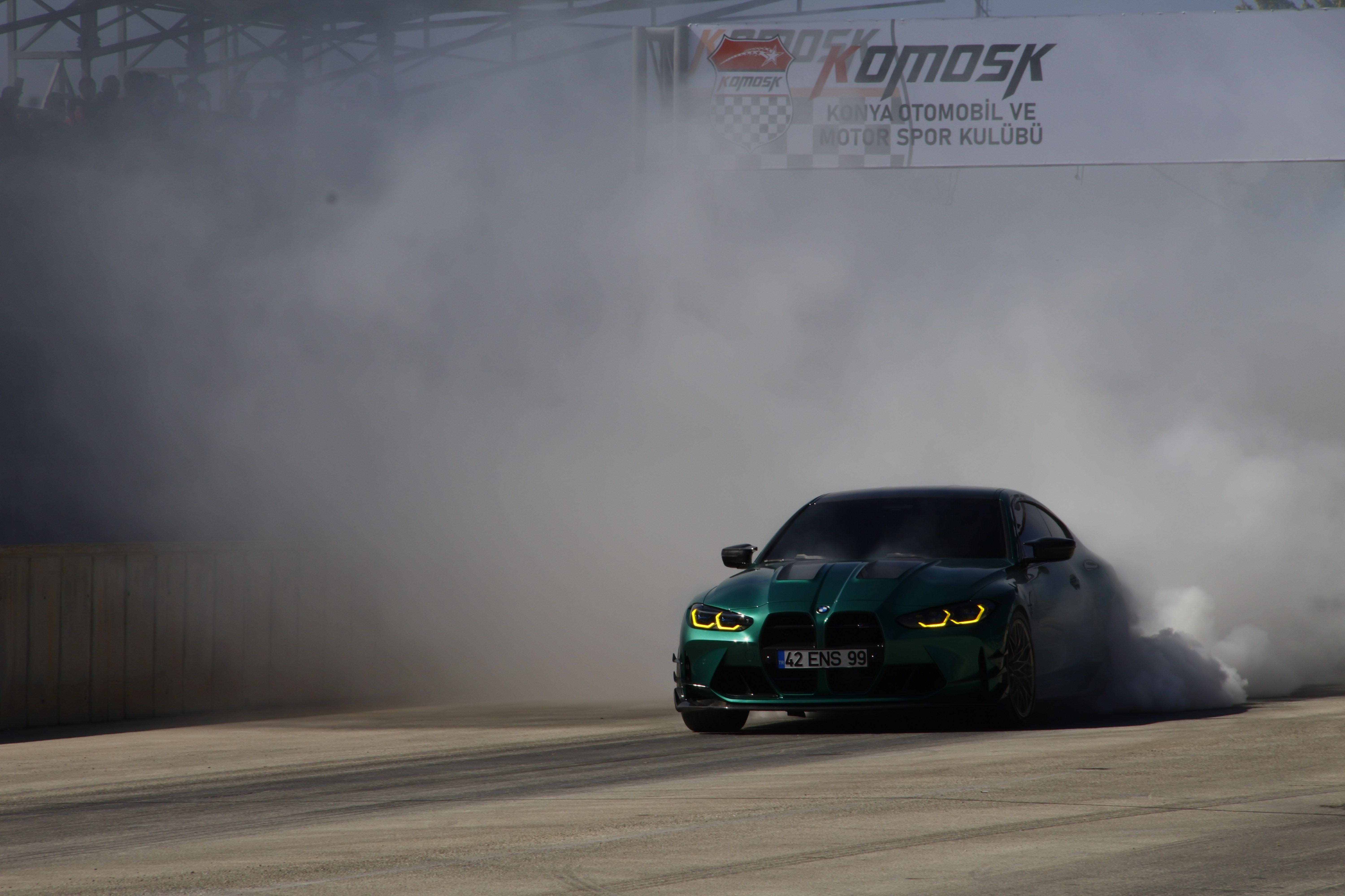 Une voiture de sport verte effectuant un drift sur une piste, entourée de fumée.
