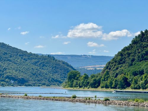 Free Beautiful river scene with lush green hills under a blue sky. Stock Photo