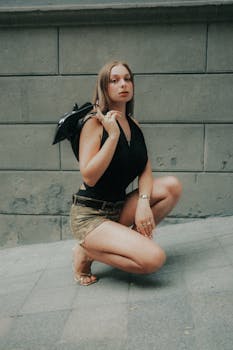 Confident woman in casual wear poses against concrete wall, showcasing urban fashion.