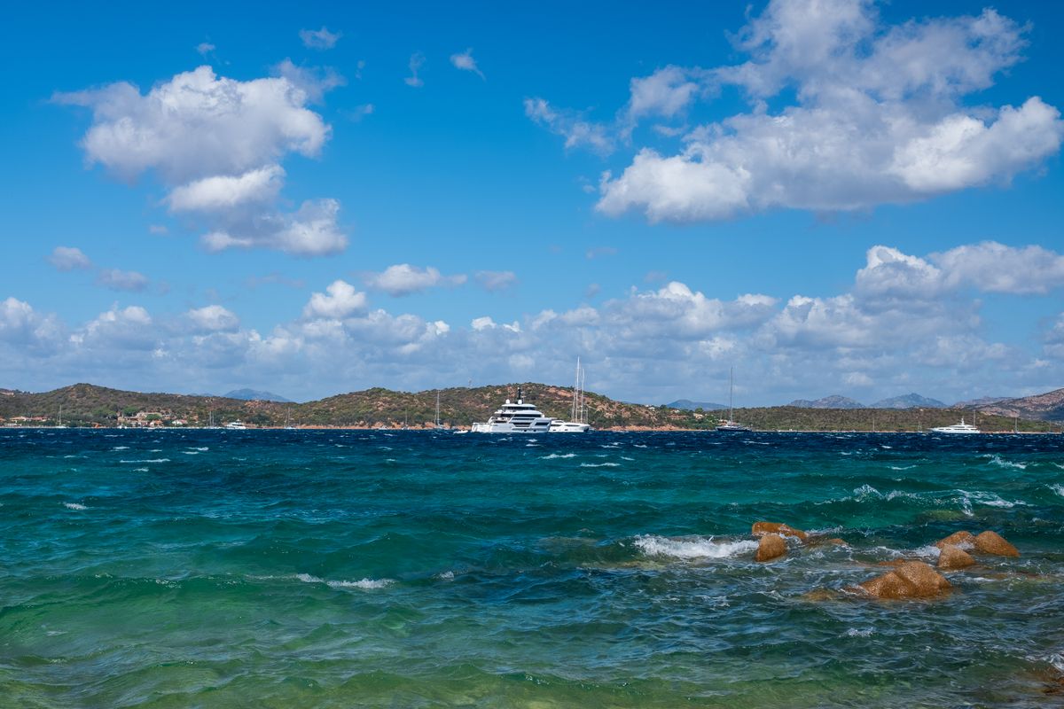 Iaht mare ancorat in larg, cu mare verde-turcoaz si stanci roscate