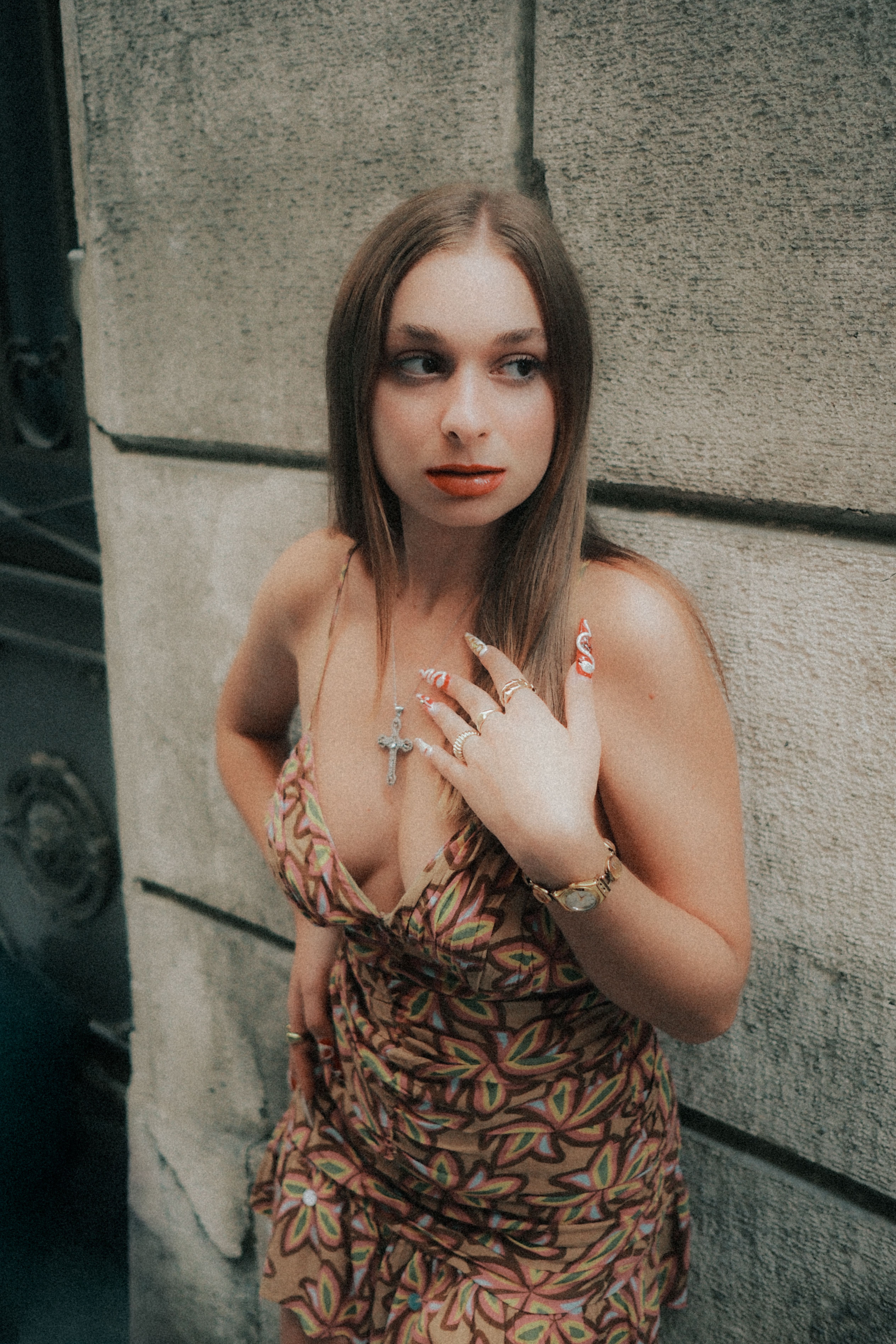 Young woman in patterned dress and jewelry poses against a stone wall.