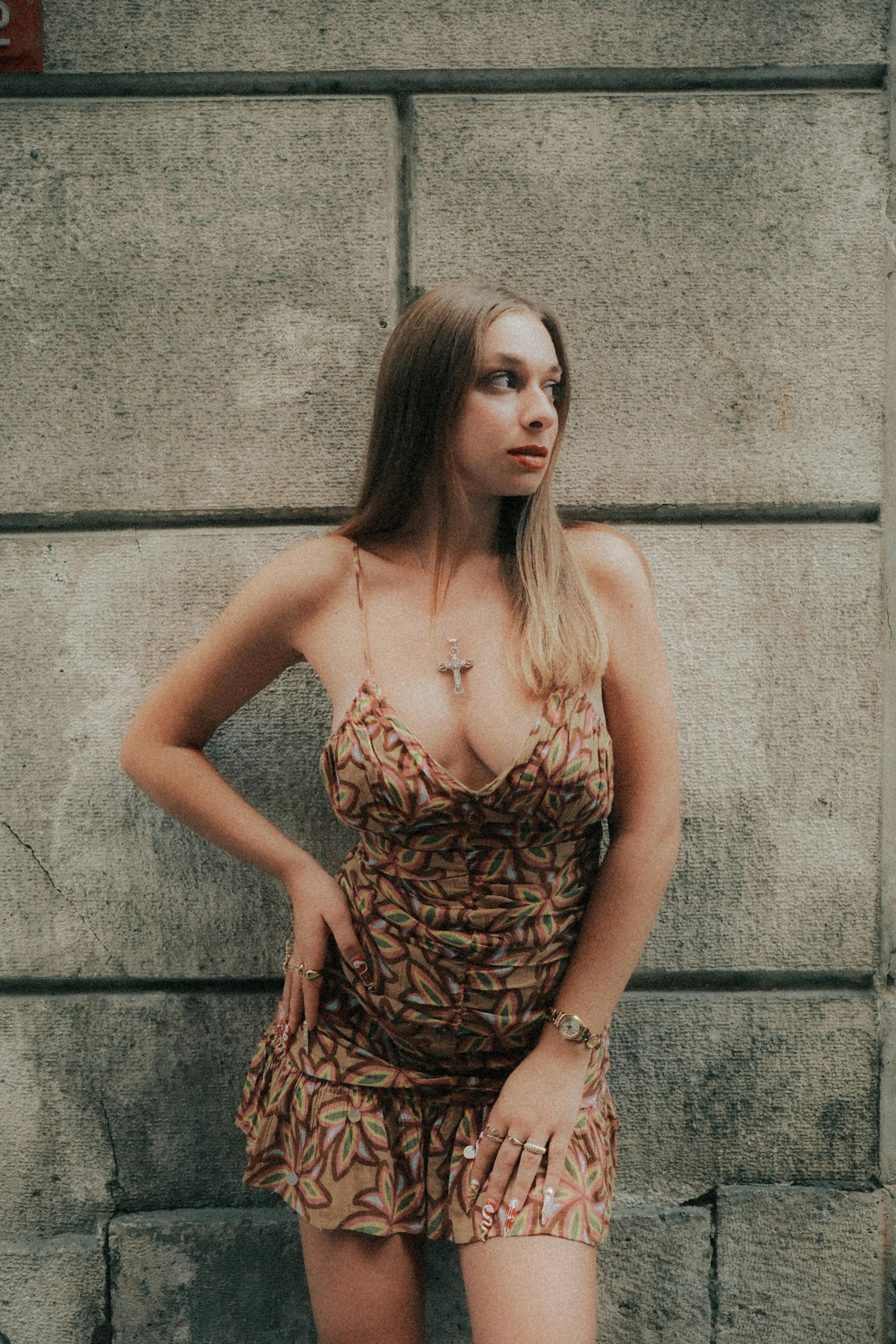 Stylish young woman poses confidently in a patterned dress against a textured urban wall.