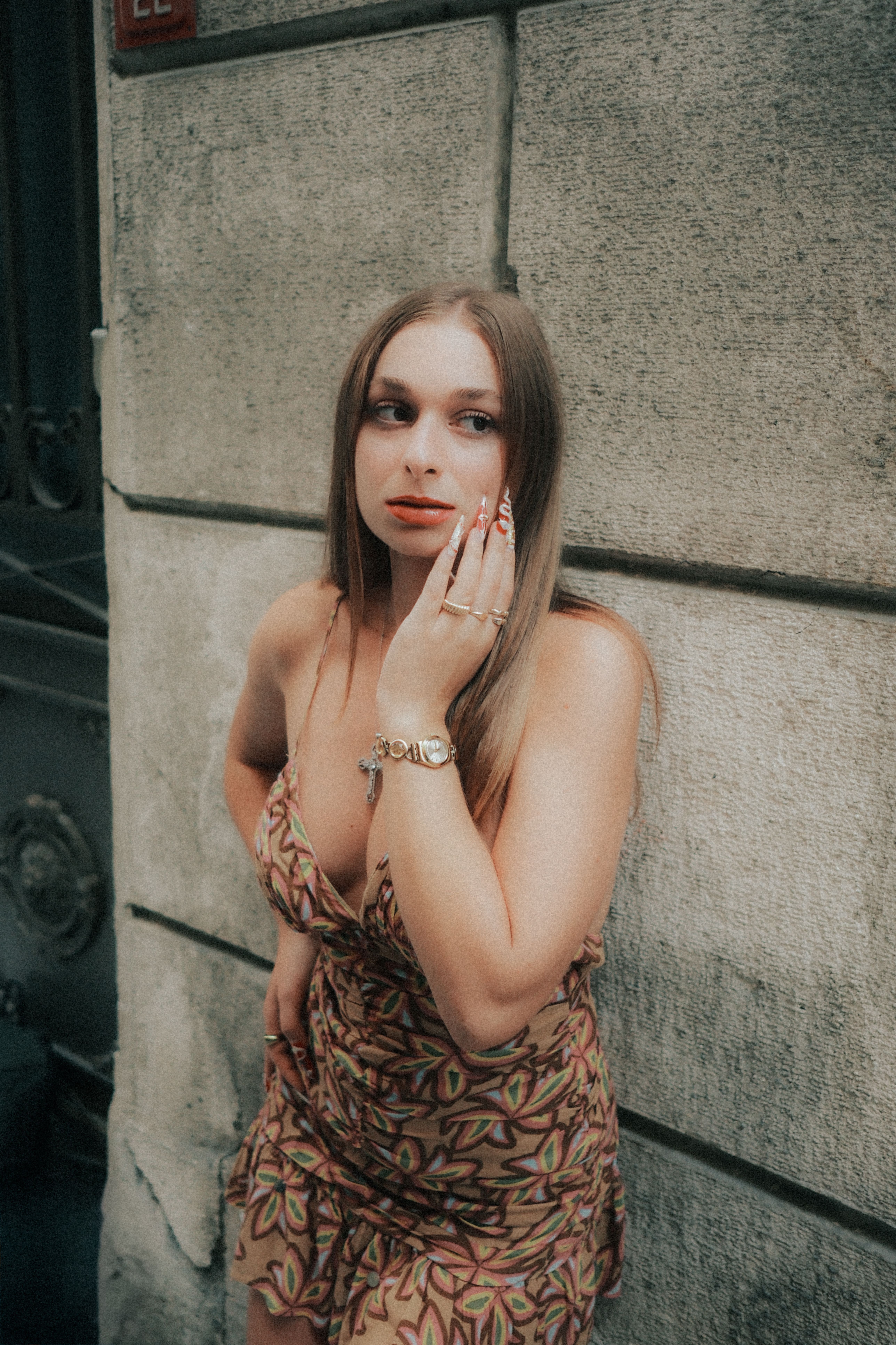 Woman in patterned dress posing by stone wall in urban street.