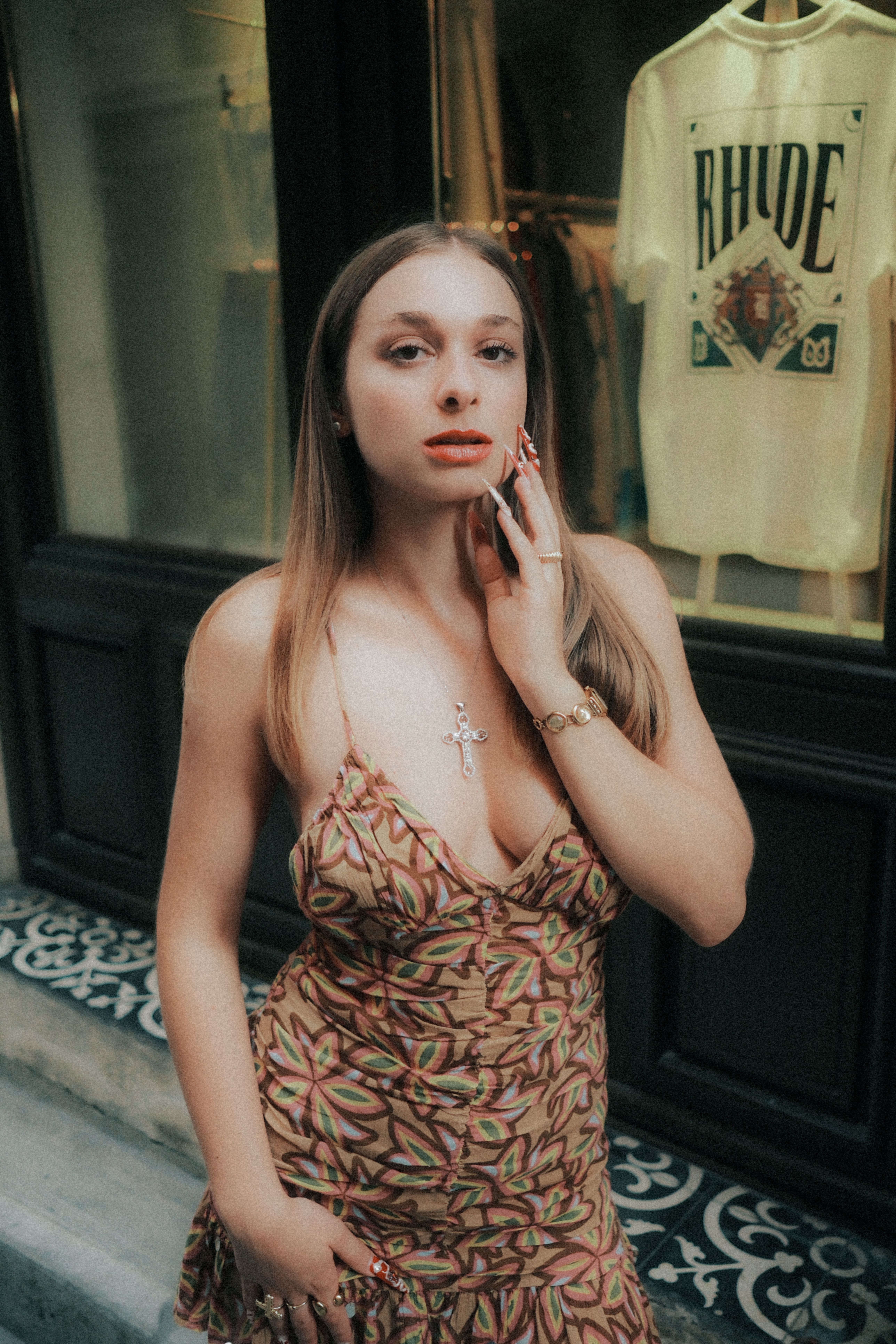 Stylish woman in a patterned dress poses confidently in front of a boutique window.