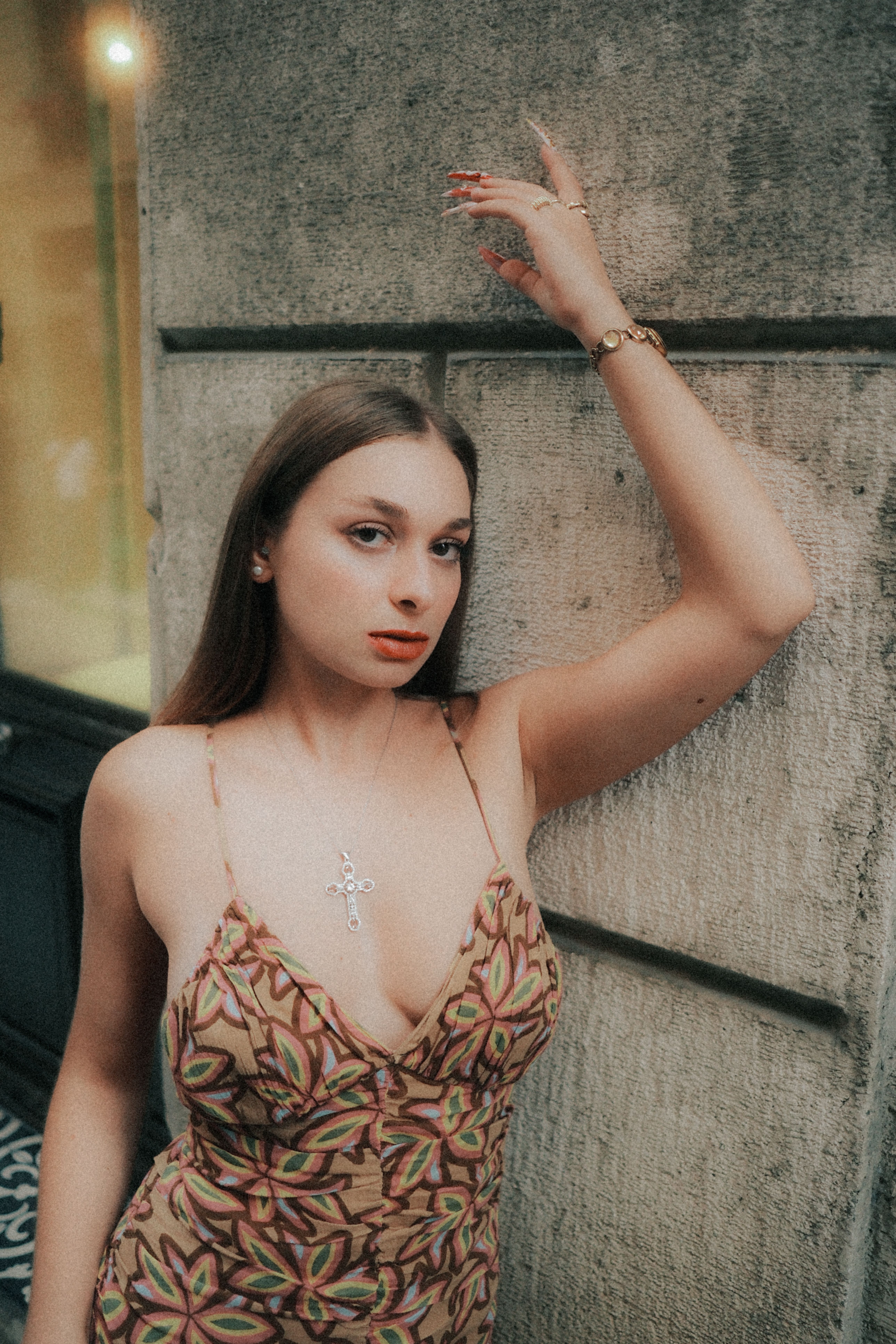 Young woman in patterned dress posing confidently against an urban wall.