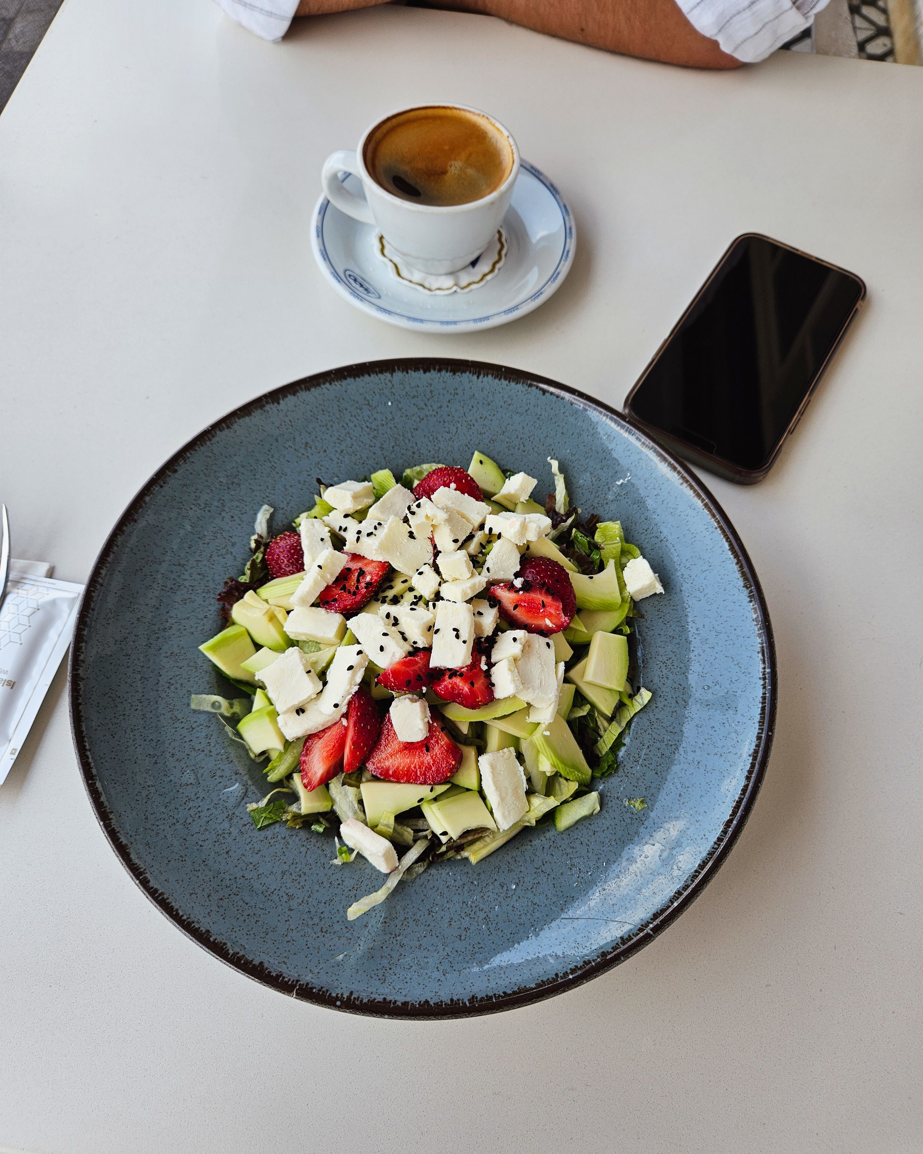 Fresh salad with feta, strawberries, avocado, and coffee on a table in Istanbul.