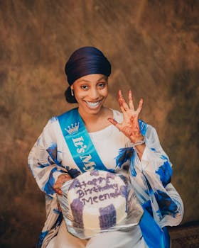 Smiling woman in Zaria, Nigeria holding birthday cake with henna art.