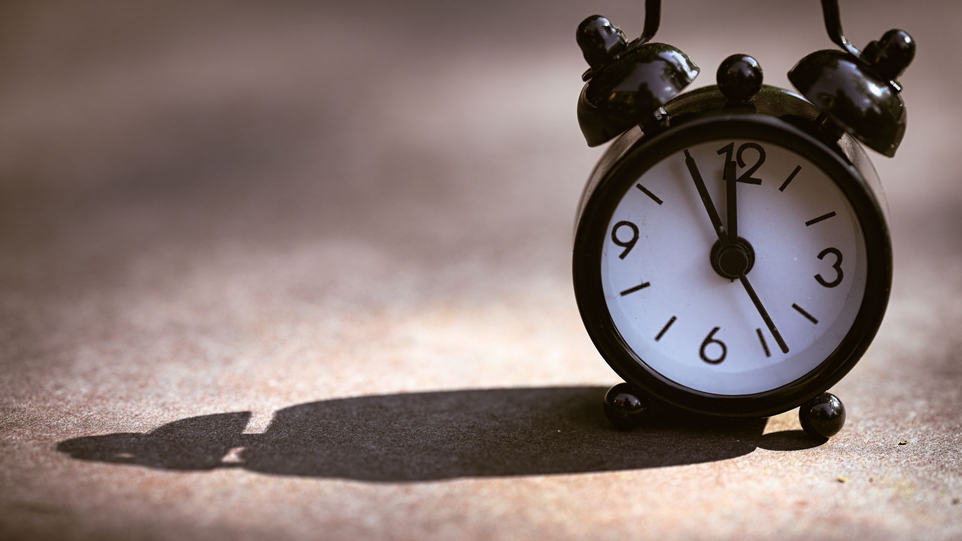 Modafinil's Wakefulness Effects: A Comprehensive Guide A classic black alarm clock showing five minutes to twelve on a textured surface with dramatic shadow.