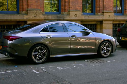 Free Stylish silver sedan parked by a brick building with blue windows on a city street. Stock Photo