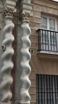 Ornate Baroque columns with unique wavy design near a balcony in Cadiz, Spain.