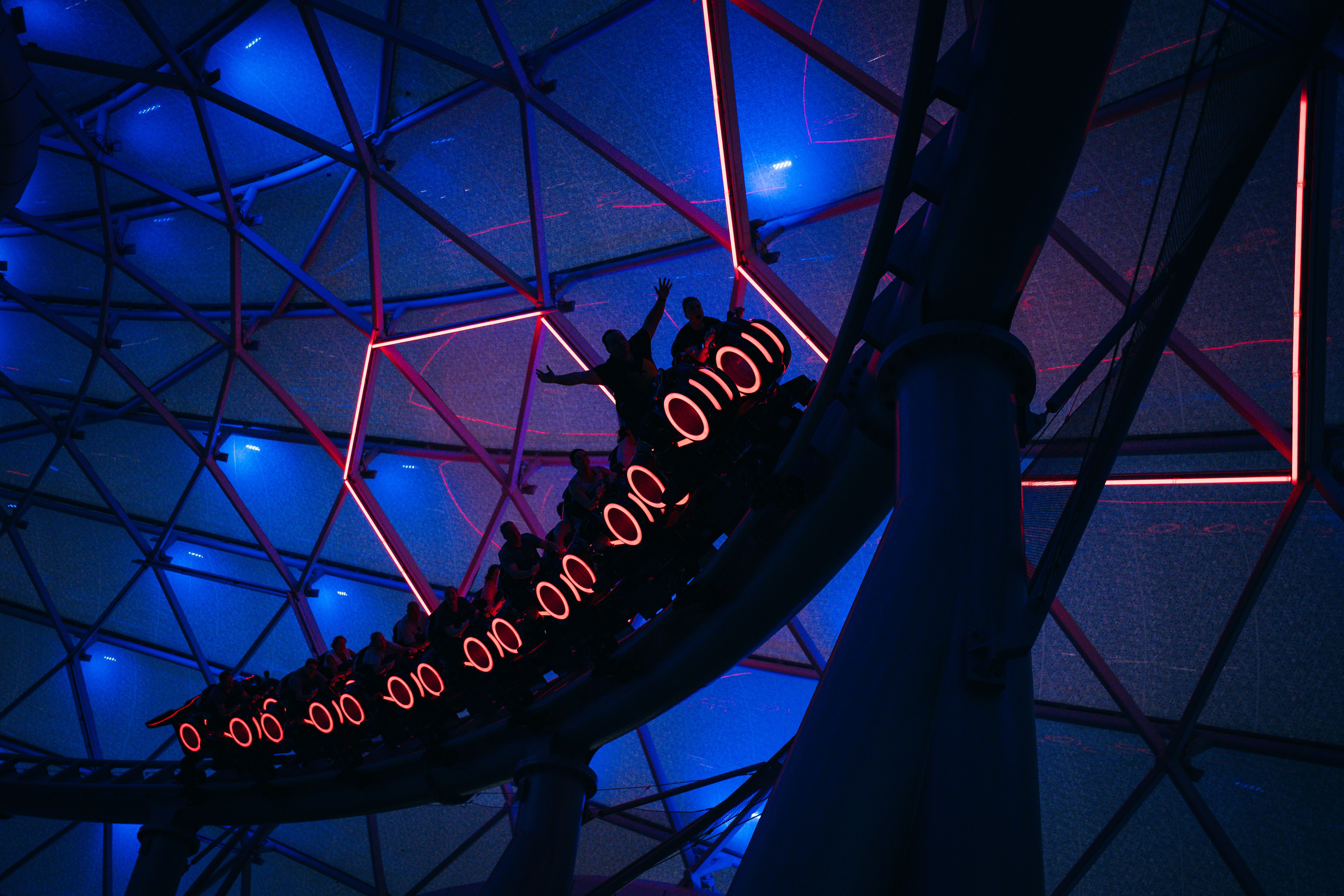 Silhouette of a roller coaster ride with neon blue and red lights creating an electric atmosphere.