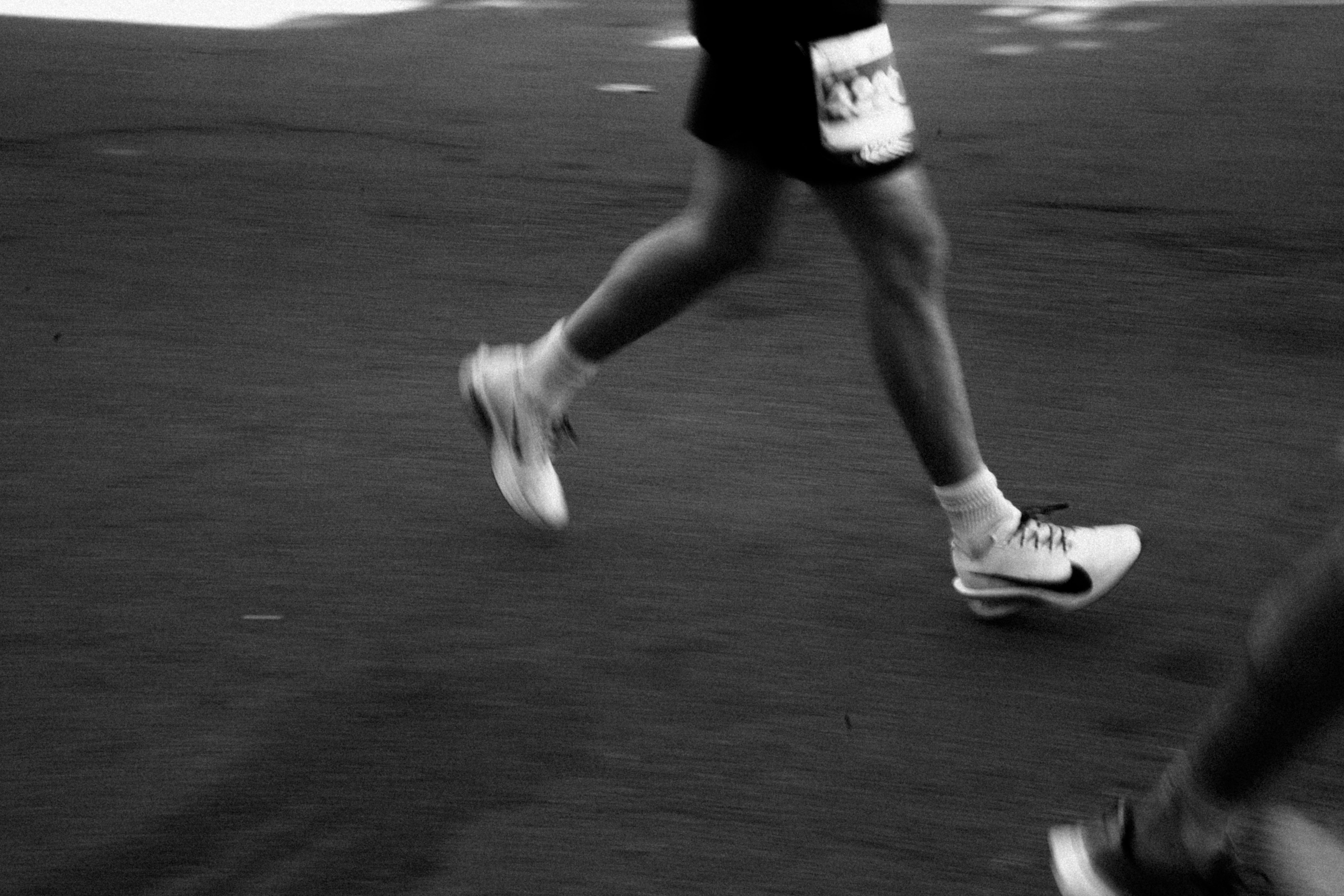 Black and white photo of a runner's legs in motion on a city street, creating a dynamic blur effect.