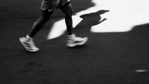 Captivating black and white image of a runner's shadow casting on the pavement in motion.