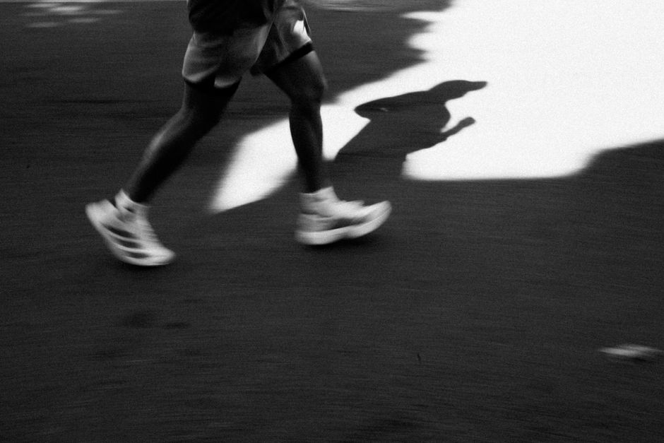 Captivating black and white image of a runner's shadow casting on the pavement in motion.