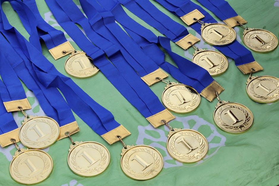 Multiple gold medals with blue ribbons arranged on a green surface, symbolizing victory.