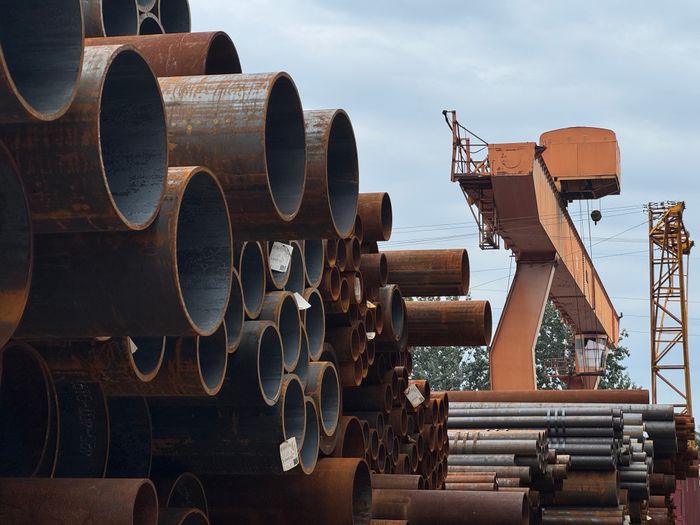 Stacked steel pipes with crane in yard