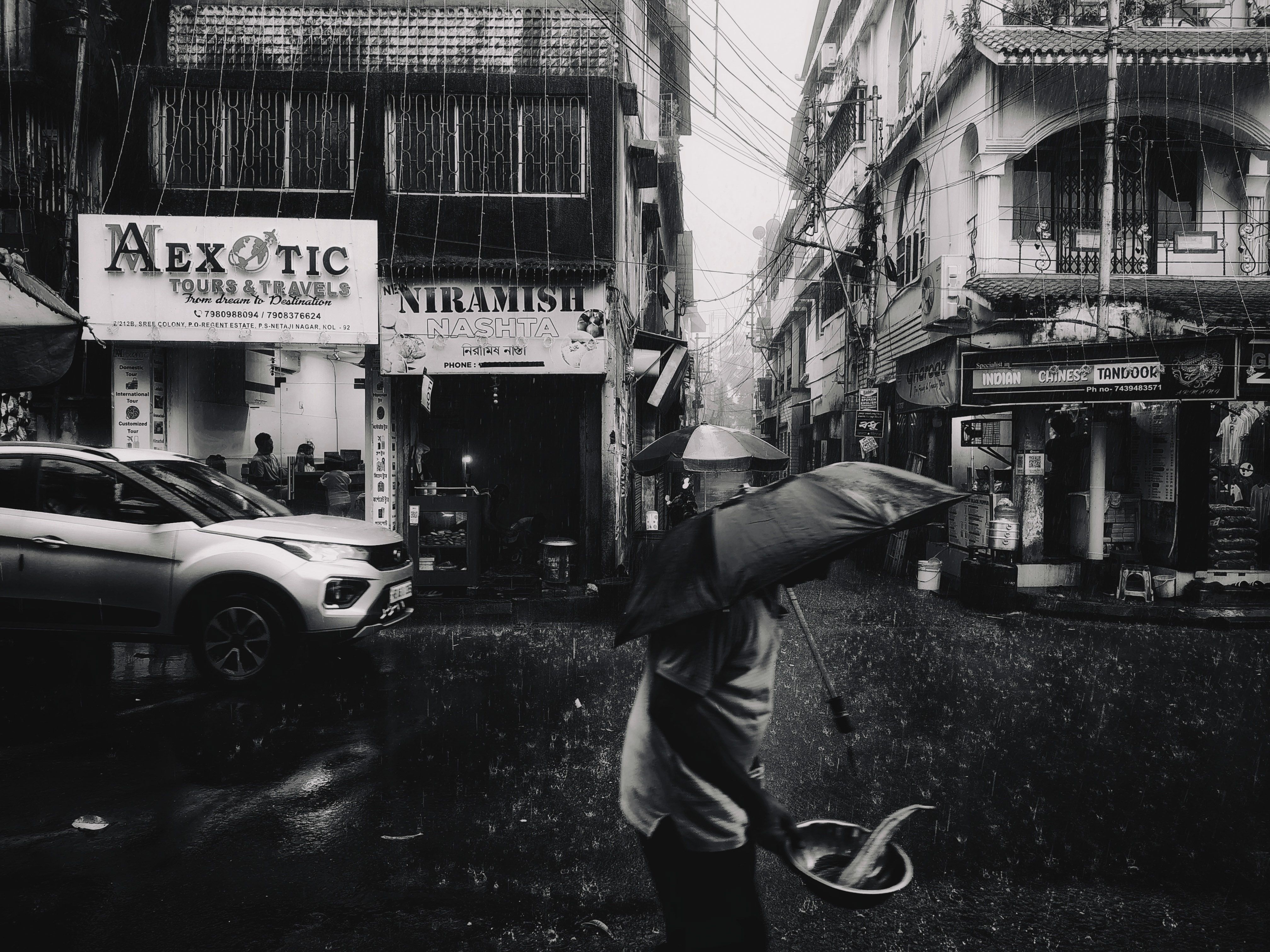 Black and white image of a bustling street in the rain, featuring pedestrians with umbrellas.
