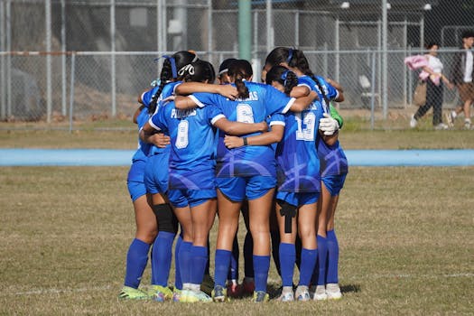 A group of female soccer players huddling in blue uniforms, preparing for the game.