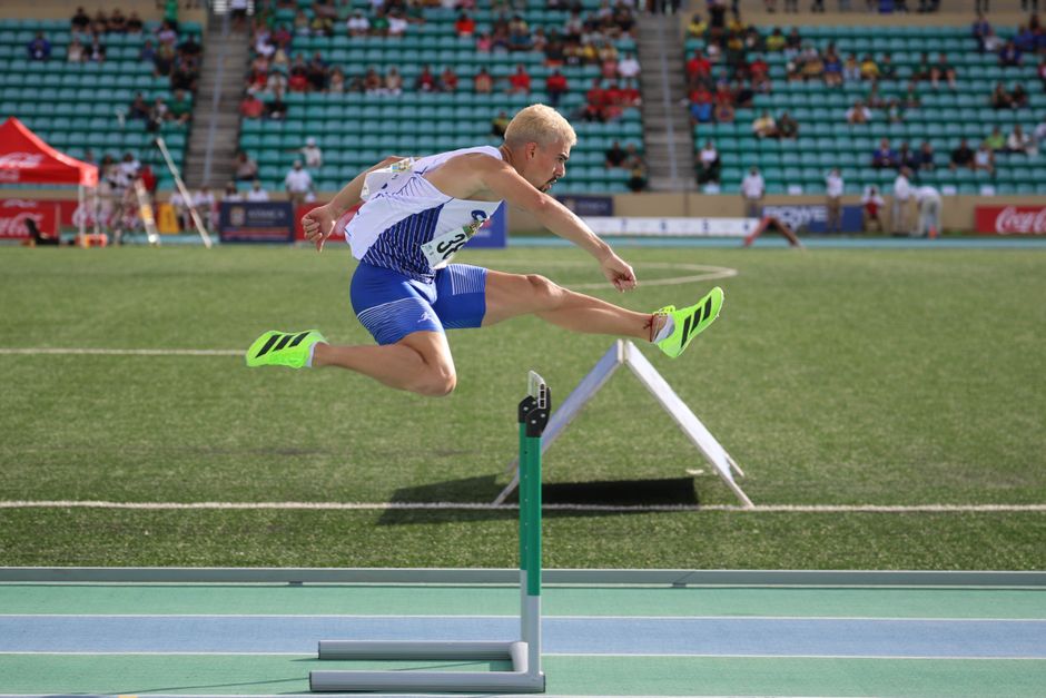 Dynamic shot of an athlete clearing a hurdle during an outdoor track event.