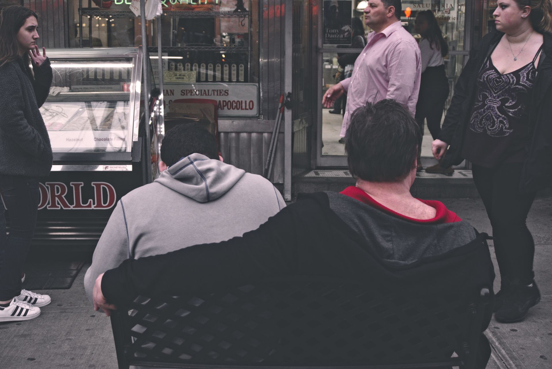 A group of people on a city street sitting and standing outside a shop.