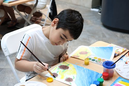 Free Child focused on painting at a table with colorful paints and brushes at an indoor art class. Stock Photo