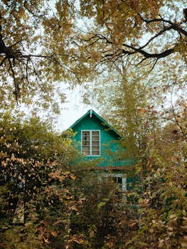 A quaint green cottage surrounded by autumn leaves, creating a tranquil outdoor scene.
