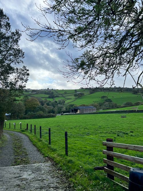 Free Serene rural scene with lush green fields and distant hills under a cloudy sky. Stock Photo